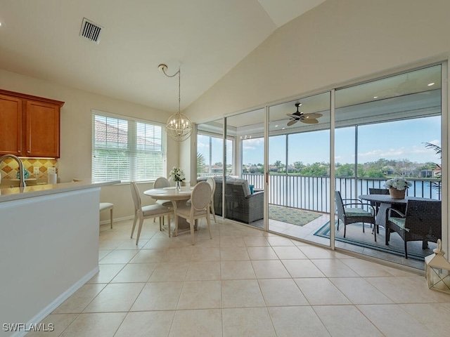 tiled dining area featuring sink, vaulted ceiling, a water view, and ceiling fan with notable chandelier