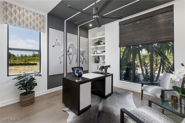 home office with dark wood-type flooring, ceiling fan, built in features, and plenty of natural light