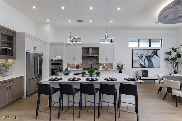 kitchen featuring a breakfast bar, pendant lighting, gray cabinetry, wall chimney exhaust hood, and stainless steel appliances