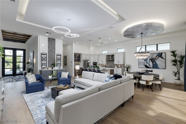 living room with french doors, light wood-style flooring, a tray ceiling, and a notable chandelier