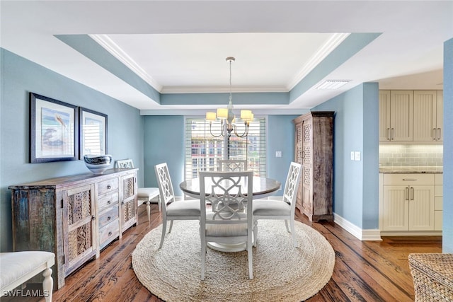 dining space featuring wood-type flooring, a raised ceiling, ornamental molding, and a notable chandelier