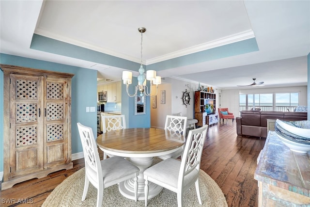 dining area with a raised ceiling, ceiling fan with notable chandelier, dark hardwood / wood-style flooring, and ornamental molding