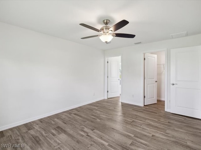 unfurnished bedroom with a spacious closet, dark hardwood / wood-style floors, a closet, and ceiling fan