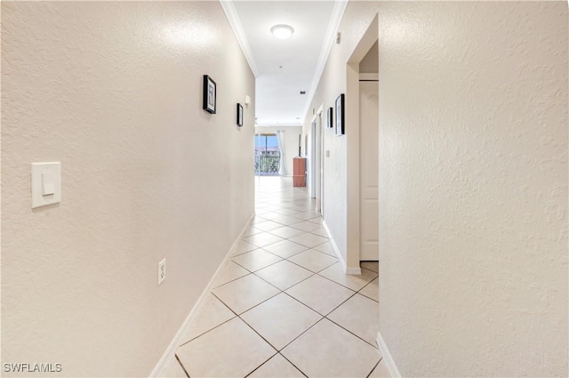 hallway featuring baseboards, a textured wall, ornamental molding, and light tile patterned flooring