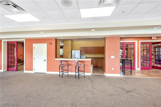 kitchen with light carpet, kitchen peninsula, a breakfast bar, a drop ceiling, and white refrigerator with ice dispenser