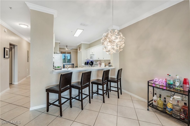 kitchen featuring white appliances, kitchen peninsula, white cabinetry, ornamental molding, and a breakfast bar