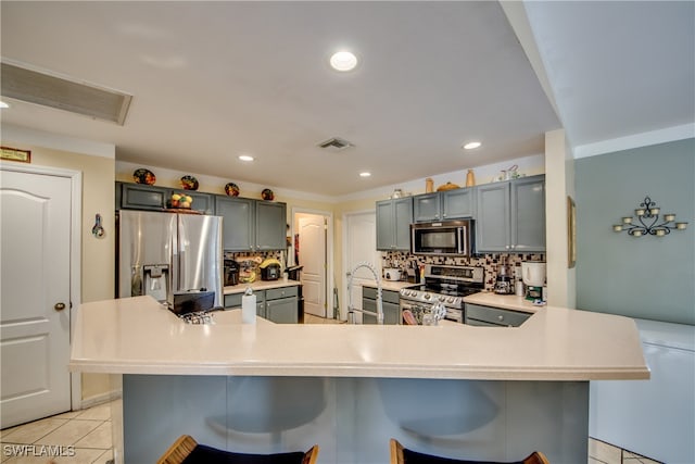 kitchen with decorative backsplash, light tile patterned floors, a kitchen bar, kitchen peninsula, and stainless steel appliances