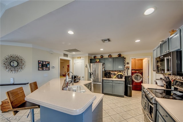 kitchen featuring a breakfast bar, stainless steel appliances, sink, washer / dryer, and light tile patterned flooring