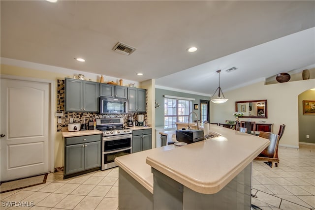 kitchen featuring a breakfast bar, lofted ceiling, a center island with sink, hanging light fixtures, and stainless steel appliances