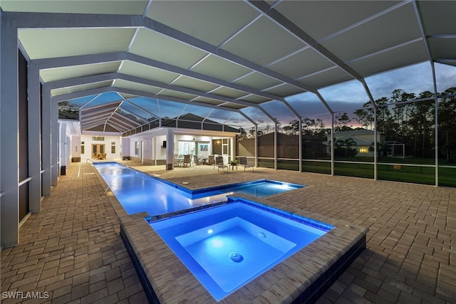 pool at dusk featuring a lanai, a patio area, and an in ground hot tub