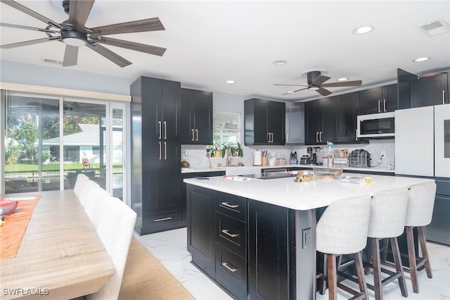 kitchen featuring white appliances, tasteful backsplash, a center island, ceiling fan, and a breakfast bar area