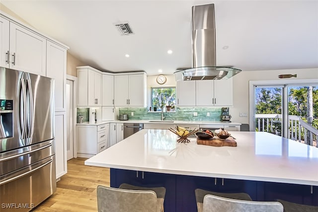 kitchen featuring white cabinets, appliances with stainless steel finishes, island range hood, light hardwood / wood-style floors, and sink