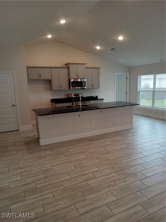 kitchen with gray cabinets, a center island with sink, vaulted ceiling, and sink