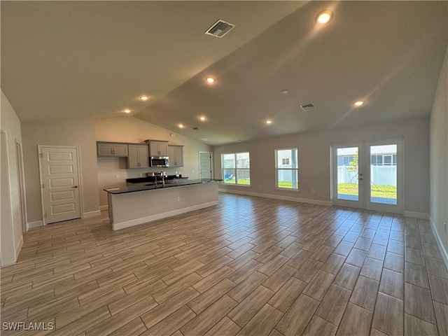 2919 NW 10th St, Cape Coral, FL 33993 - kitchen with open floor plan, stainless steel microwave, dark countertops, vaulted ceiling, and wood tiled floors