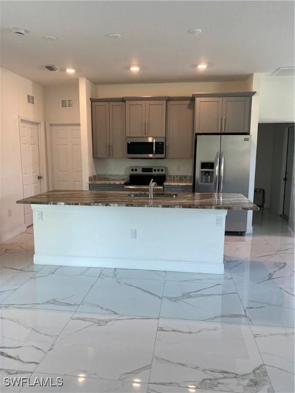 kitchen with sink, a center island with sink, dark stone counters, and stainless steel appliances