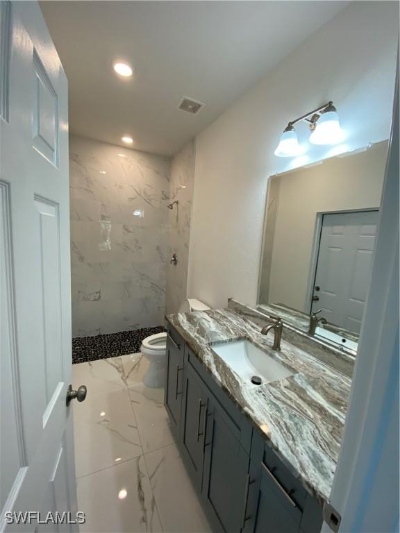 bathroom featuring toilet, vanity, and a tile shower