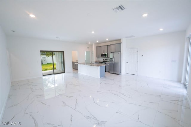 kitchen with an island with sink, gray cabinetry, light stone countertops, and stainless steel appliances