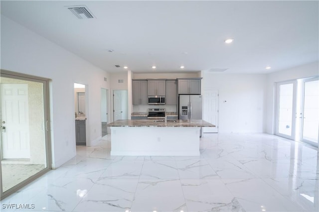 kitchen featuring stone countertops, appliances with stainless steel finishes, gray cabinets, a kitchen island with sink, and a breakfast bar area