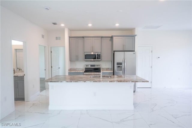 kitchen featuring stainless steel appliances, sink, a kitchen island with sink, light stone counters, and gray cabinetry