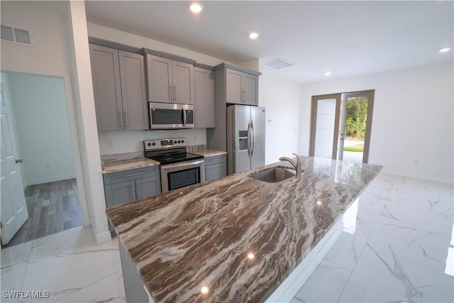 kitchen with sink, a center island with sink, appliances with stainless steel finishes, and gray cabinetry