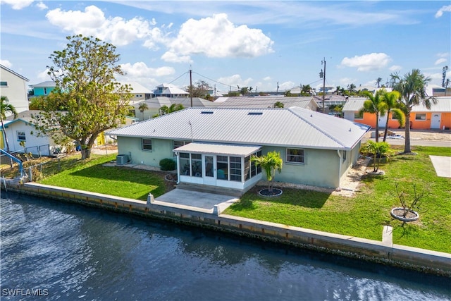 rear view of property featuring a patio area, a sunroom, a lawn, and a water view