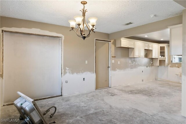 interior space featuring concrete flooring, white cabinets, hanging light fixtures, a notable chandelier, and a textured ceiling