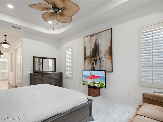 bedroom with multiple windows, a raised ceiling, ensuite bath, and ceiling fan