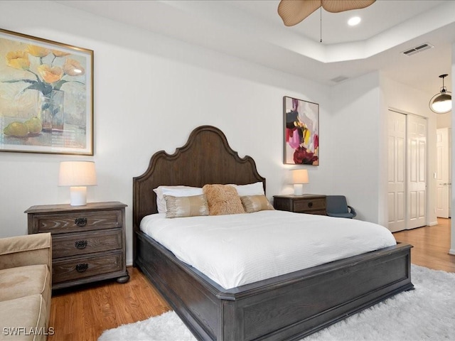 bedroom with a raised ceiling, ceiling fan, a closet, and light hardwood / wood-style flooring