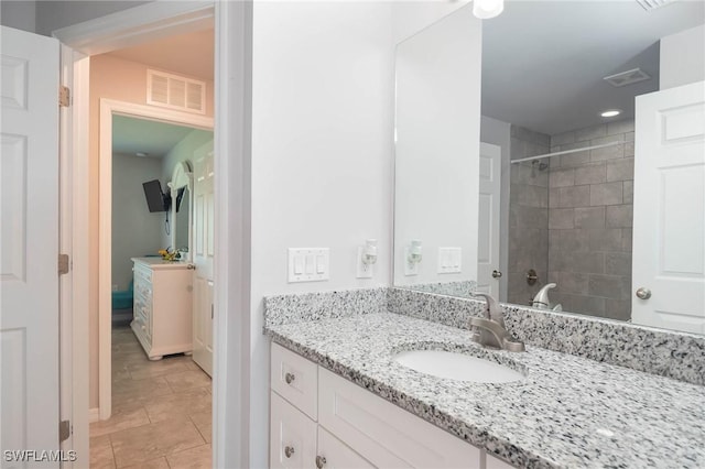 bathroom with tile patterned flooring, a tile shower, and vanity