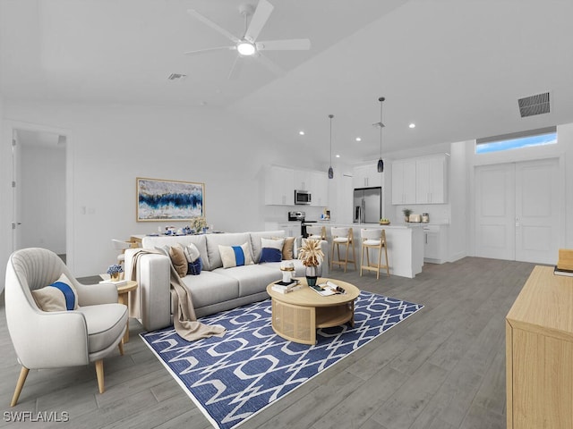 living room with ceiling fan, light hardwood / wood-style floors, and vaulted ceiling