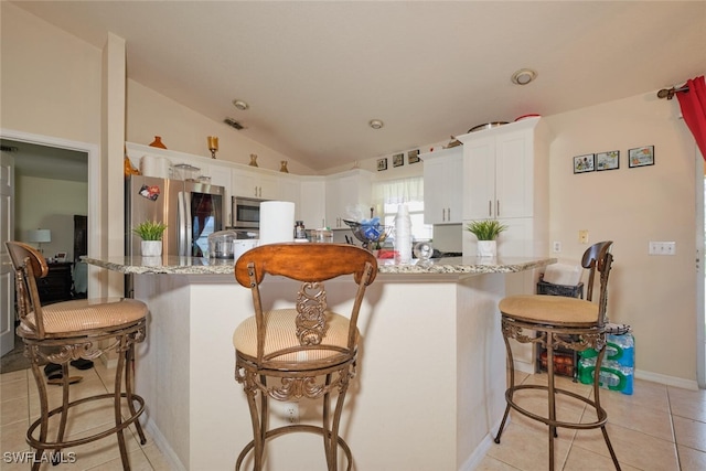 kitchen with white cabinetry, stainless steel appliances, light stone counters, and vaulted ceiling