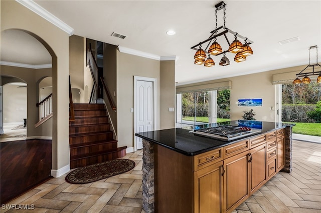 kitchen with a center island, pendant lighting, stainless steel gas stovetop, dark stone countertops, and crown molding