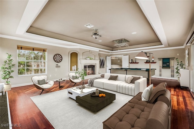 living room with ceiling fan, a tray ceiling, dark hardwood / wood-style flooring, and crown molding