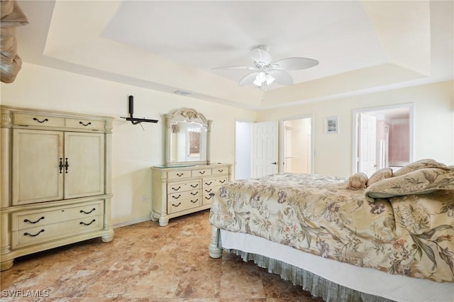 bedroom with connected bathroom, multiple windows, a tray ceiling, and ceiling fan