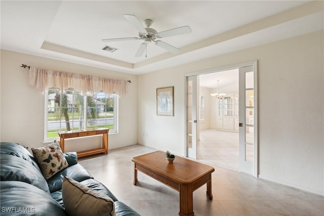 living room with ceiling fan with notable chandelier and a raised ceiling