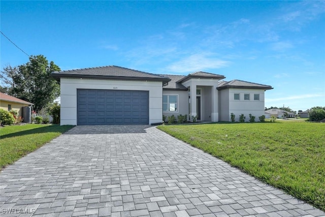 prairie-style home featuring decorative driveway, an attached garage, stucco siding, and a front yard