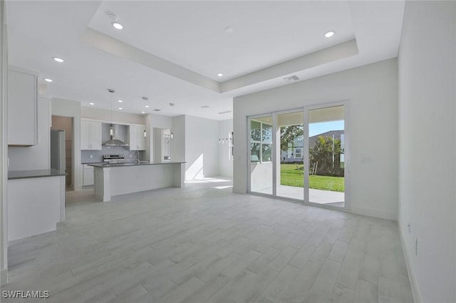 unfurnished living room with recessed lighting, light wood-type flooring, a raised ceiling, and baseboards