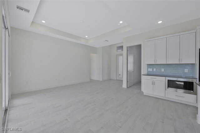 kitchen with visible vents, open floor plan, tasteful backsplash, stainless steel microwave, and a raised ceiling