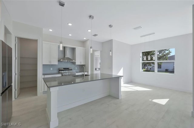 kitchen with stainless steel appliances, dark countertops, white cabinetry, a sink, and wall chimney exhaust hood