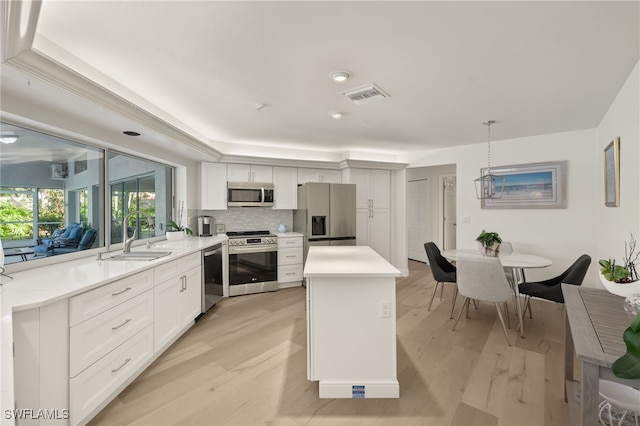 kitchen featuring appliances with stainless steel finishes, white cabinetry, decorative light fixtures, and sink