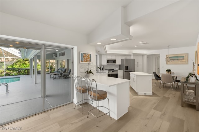 kitchen with decorative backsplash, a breakfast bar area, kitchen peninsula, stainless steel appliances, and white cabinetry