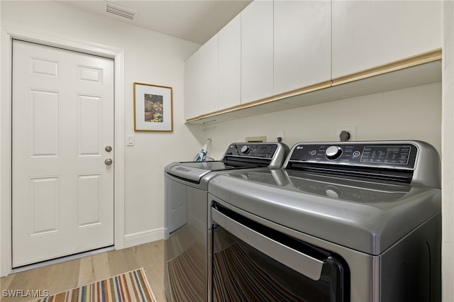 clothes washing area with light hardwood / wood-style flooring, independent washer and dryer, and cabinets