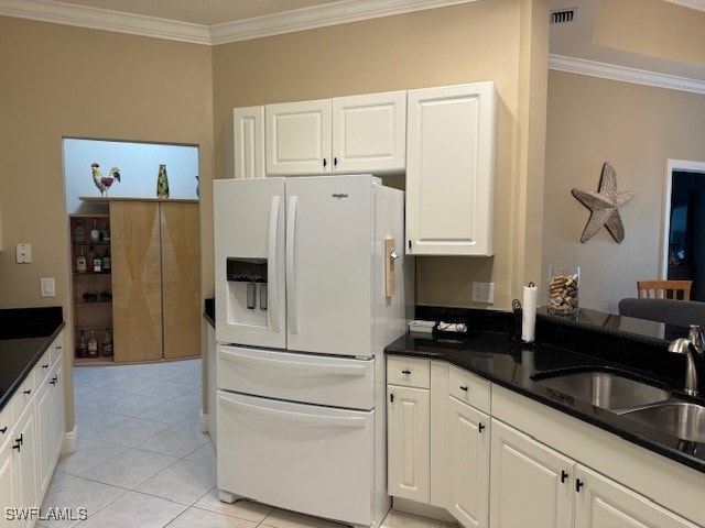 kitchen with white fridge with ice dispenser, crown molding, white cabinets, and light tile patterned flooring