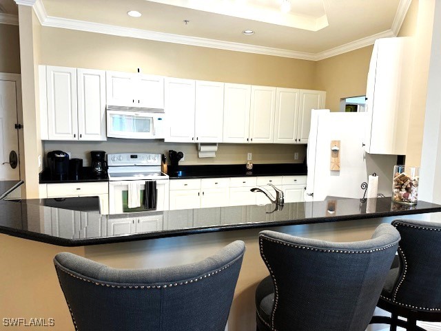 kitchen with a breakfast bar area, kitchen peninsula, white cabinetry, and white appliances