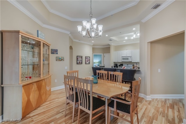 dining space with a raised ceiling, ornamental molding, and light hardwood / wood-style flooring