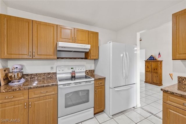 kitchen featuring light tile patterned floors, dark stone counters, and white appliances