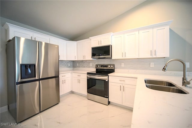 kitchen with lofted ceiling, white cabinets, light stone counters, appliances with stainless steel finishes, and sink