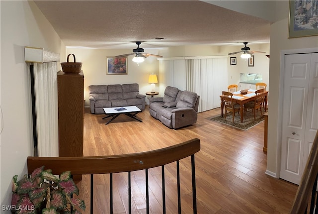 living room with ceiling fan, wood-type flooring, and a textured ceiling