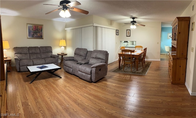 living room featuring wood-type flooring, a textured ceiling, and ceiling fan