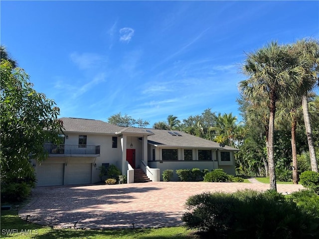 single story home featuring an attached garage, a balcony, decorative driveway, and stucco siding